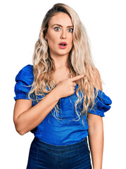 Wall Mural - Young blonde woman wearing casual clothes surprised pointing with finger to the side, open mouth amazed expression.