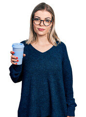 Young blonde woman drinking a take away cup coffee thinking attitude and sober expression looking self confident