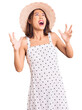 Young beautiful chinese girl wearing summer hat crazy and mad shouting and yelling with aggressive expression and arms raised. frustration concept.