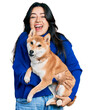 Beautiful hispanic woman holding cute dog celebrating crazy and amazed for success with open eyes screaming excited.