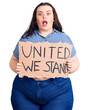 © Krakenimages.com - Young plus size woman holding united we stand banner scared and amazed with open mouth for surprise, disbelief face