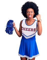 Poster - Young african american woman wearing cheerleader uniform holding pompom angry and mad raising fist frustrated and furious while shouting with anger. rage and aggressive concept.