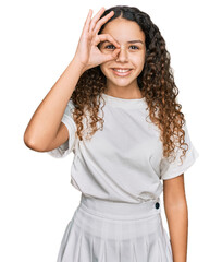 Teenager hispanic girl wearing casual white t shirt smiling happy doing ok sign with hand on eye looking through fingers