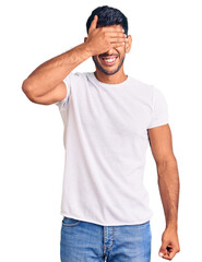 Sticker - Young latin man wearing casual clothes smiling and laughing with hand on face covering eyes for surprise. blind concept.