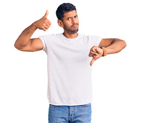 Sticker - Young latin man wearing casual clothes doing thumbs up and down, disagreement and agreement expression. crazy conflict