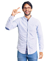 Poster - Handsome hispanic man wearing business shirt and glasses smiling and confident gesturing with hand doing small size sign with fingers looking and the camera. measure concept.