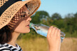 Young woman in straw hat drinking water outdoors on hot summer day. Refreshing drink