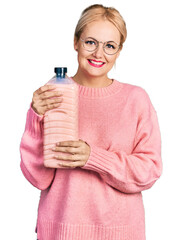 Canvas Print - Young blonde woman holding detergent bottle smiling with a happy and cool smile on face. showing teeth.