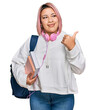 © Krakenimages.com - Hispanic woman with pink hair wearing student backpack and headphones smiling with happy face looking and pointing to the side with thumb up.
