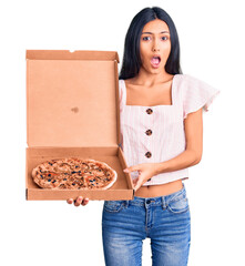 young beautiful latin girl holding delivery pizza box scared and amazed with open mouth for surprise