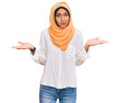 © Krakenimages.com - Young brunette woman wearing traditional islamic hijab scarf clueless and confused expression with arms and hands raised. doubt concept.