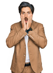 Wall Mural - Young hispanic man wearing business clothes afraid and shocked, surprise and amazed expression with hands on face