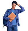 © Krakenimages.com - Young african american man wearing student backpack holding book confuse and wondering about question. uncertain with doubt, thinking with hand on head. pensive concept.