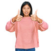 © Krakenimages.com - Beautiful young asian woman wearing casual winter sweater approving doing positive gesture with hand, thumbs up smiling and happy for success. winner gesture.