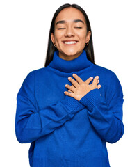 Wall Mural - Young asian woman wearing casual winter sweater smiling with hands on chest with closed eyes and grateful gesture on face. health concept.