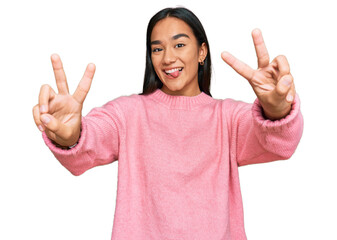 Wall Mural - Young asian woman wearing casual winter sweater smiling with tongue out showing fingers of both hands doing victory sign. number two.