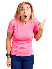 Poster - Young blonde woman wearing sportswear surprised pointing with hand finger to the side, open mouth amazed expression.