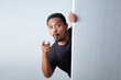 man peeking behind wall while pointing finger