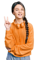 Poster - Young brunette girl with long hair wearing sweatshirt and headphones smiling with happy face winking at the camera doing victory sign. number two.