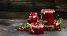 Fresh Red Cherries Fruit On Wooden Background. Jar Of Cherry Jam And Sour Cherries. Berries Cherry With Syrup. Canned Fruit. Place For Text, Top View