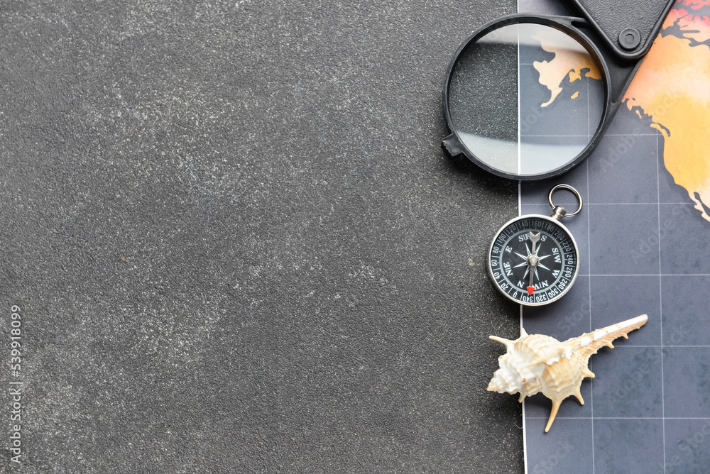 Magnifier, compass, seashell and world map on dark background