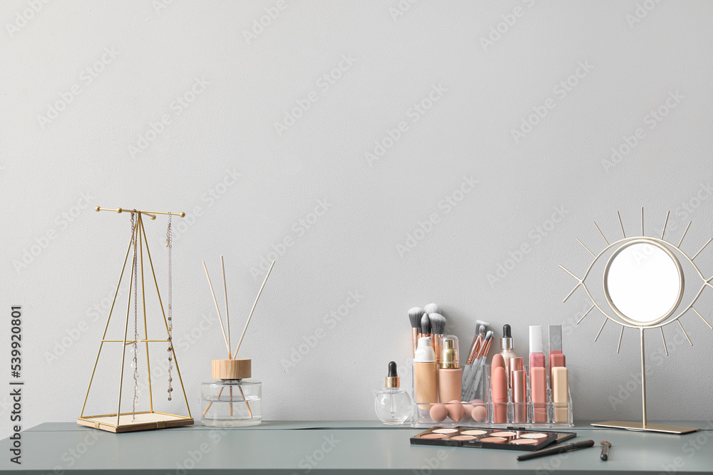 Organizer with decorative cosmetics, mirror, reed diffuser and jewelry on table near light wall