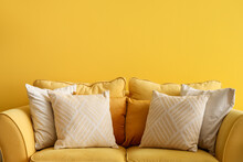 Yellow sofa with cushions near color wall in living room