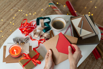 Woman hands are packing christmas postcard, gift card to the envelope. Concept.