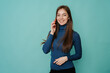 © Iona - Attractive cheerful young blonde woman in blue sweater making call, using phone, looking at camera, toothy smiling over turquoise studio background with copy space. Promo, mockup of communication.