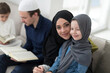 © .shock - Traditional muslim family parents with children reading Quran and praying together on the sofa before iftar dinner during a ramadan feast at home