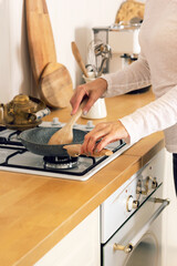 Woman with close-up hands cooks in the kitchen at the stove. A frying pan and other dishes in the frame. Scandinavian style