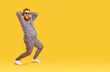 Crazy funny fat man with big belly in pajama suit with leopard print is dancing and fooling around. Cheerful chubby bearded freak man in sunglasses laughing loudly on orange background. Full length.