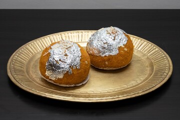 Closeup of two silver-decorated Laddu cookies on a gold plate with a black background