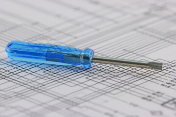 A screwdriver with a blue handle on an electrical diagram in close-up.