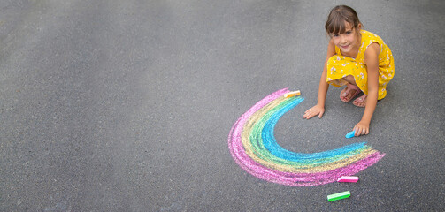 Wall Mural - A child draws a rainbow on the asphalt. Selective focus.