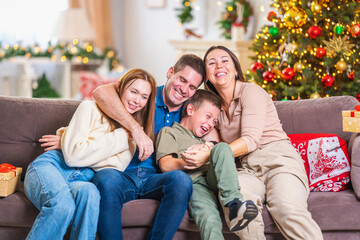 Merry Christmas. A happy loving family is sitting on the couch and having fun during the New Year holidays. Parents and children hug each other, are in the living room decorated for the holiday.