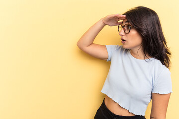 young indian woman isolated on yellow background looking far away keeping hand on forehead.