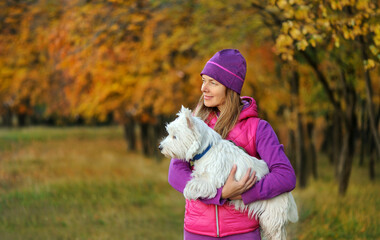 Wall Mural - Side view picture of a sportive woman holding her dog in hands