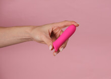 Female hand holding a clitoral vibrator on a pink background