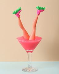 Creative layout, cocktail glass with neon slime and doll leggs on two tone pastel background. Visual trend. Minimalistic aesthetic still life. Party concept.