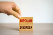 Hand puts blocks with the words Bipolar Disorder - manic depression. Mood disorder characterized by periods of depression and periods of elevated happiness. Mental disorder concept. Selective focus
