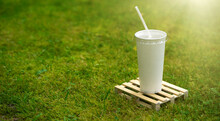 A White Glass With A Drink Stands On A Wooden Construction Pallet. Wooden Pallet For Cargo With Lemonade In A Cup.Advertising Drinks. Sale Of Refreshing Juices. A Tube In A Glass Of Juice.