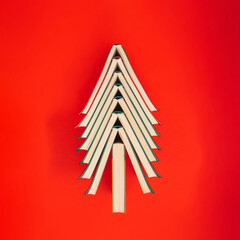 Colorful books arranged in the shape of a Christmas tree on vibrant red background. Creative Chirstmas scene in a minimalist style. Holiday book sale or black friday concept.