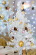 White Christmas tree with pink and gold balls and decorations. Interior. Background of shiny silver tinsel and lights.