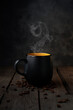 Cup of hot drink with smoke. Black coffee mug on wooden table.