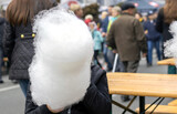 Fototapeta  - kid child boy eating cotton candy city day festival many lot of people in background walking in middle of street road celebrating. street food national holiday.white cotton candy cover child face 