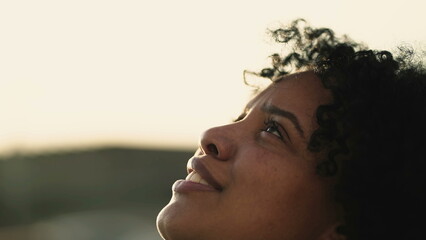 One hopeful young black woman closeup face opening eyes to sky. Religious Spiritual African American female person staring up with HOPE and FAITH