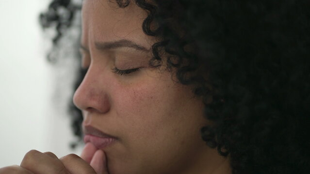 One spiritual young black woman face in prayer. Meditative contemplative Brazilian adult girl praying. Person having HOPE