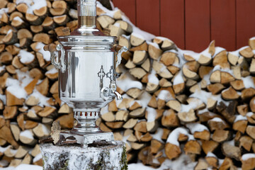 Traditional Russian samovar. A classic metal samovar against the background of a stack of firewood. Tea tradition in a village in Russia. Rural lifestyle. Nostalgic mood. Winter in the countryside.