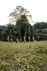 Wall Mural - A Group of Asian people with golden dance costumes pose on the green grass in front of the jungle